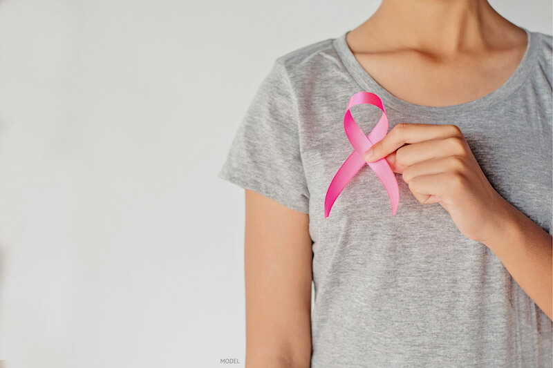 Woman holding a pink breast cancer ribbon in front of chest.